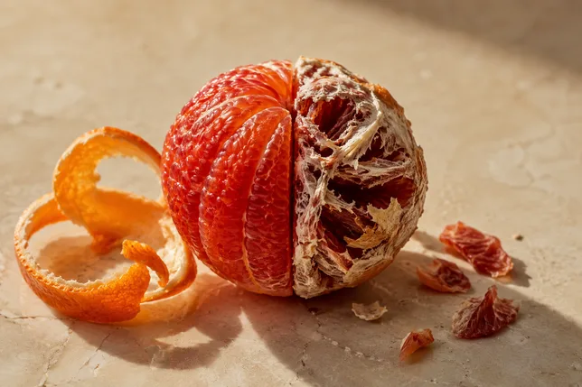 A blood orange peeled perfectly on one side and stripped too far on the other, a visual for over-exfoliation